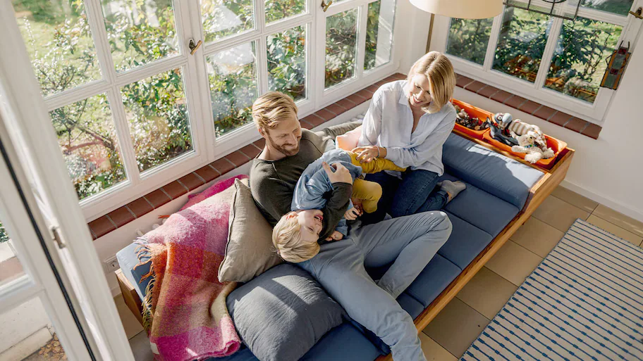 The image depicts a sunroom filled with natural light, featuring large windows that span from floor to ceiling.