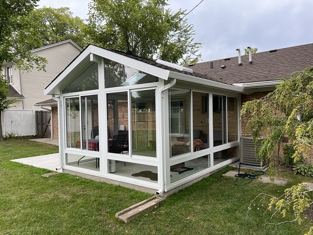 Sun-filled sunroom with large panoramic windows revealing a lush garden, comfortable wicker furniture in warm neutral tones, and an array of green indoor plants enhancing the natural ambiance.